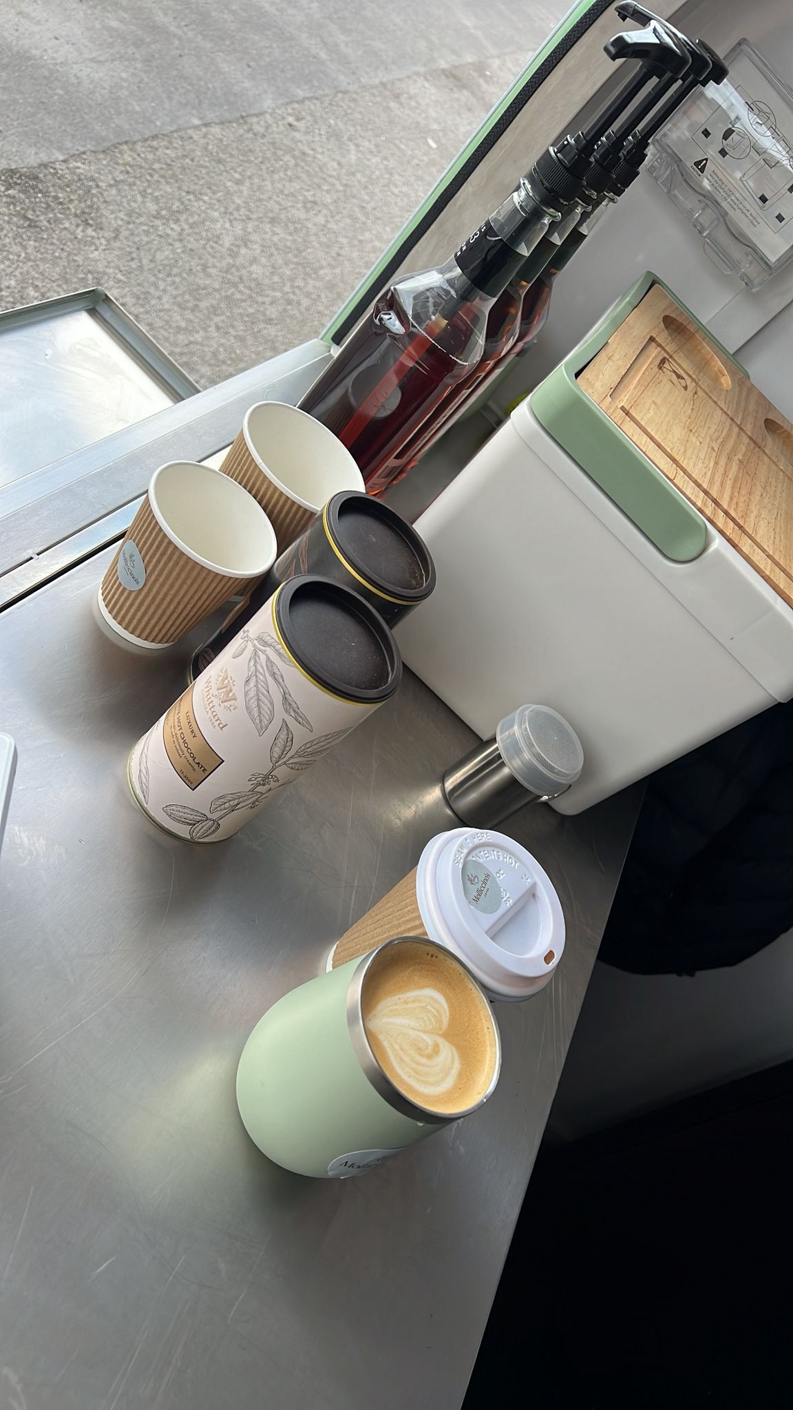 Freshly made latte with heart art in a sage green reusable cup on the trailer counter