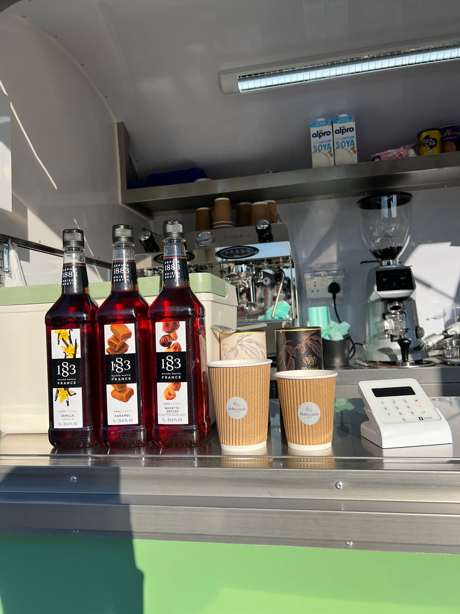 1883 Vanilla, Caramel and Hazelnut syrups lined up with Molliccino's branded cups inside the trailer