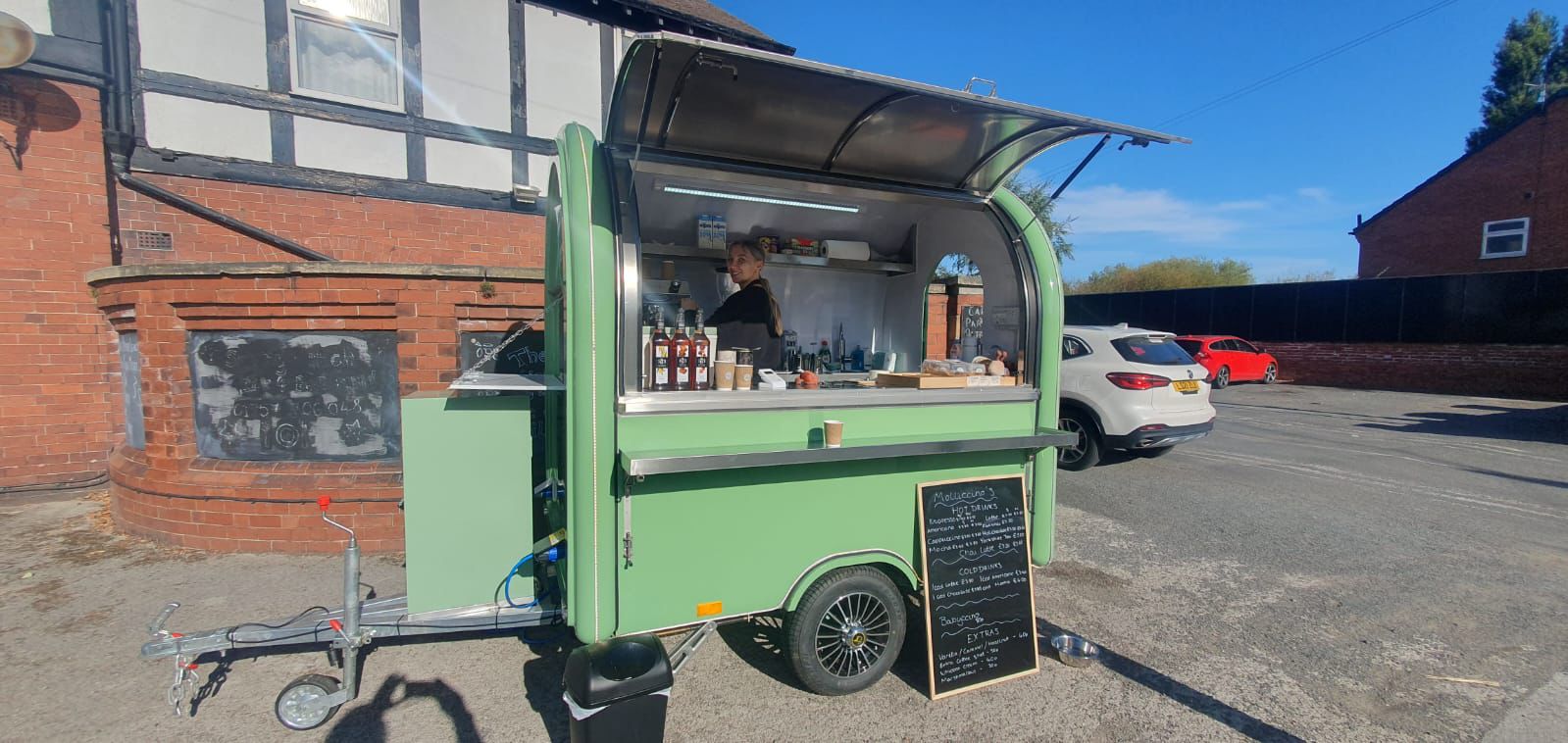 Molliccino's green coffee trailer on a sunny day with the menu chalkboard